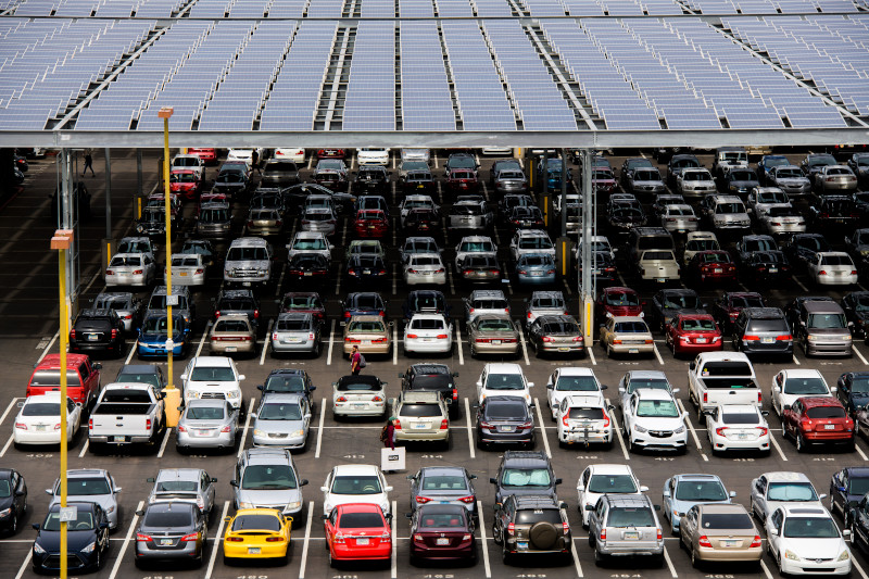 Parking lot with solar panels is filled with cars of various colors.