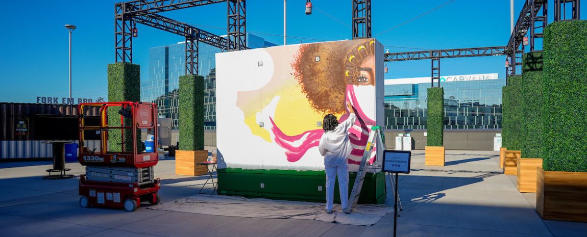 muralist painting a large wall on an outdoor structure