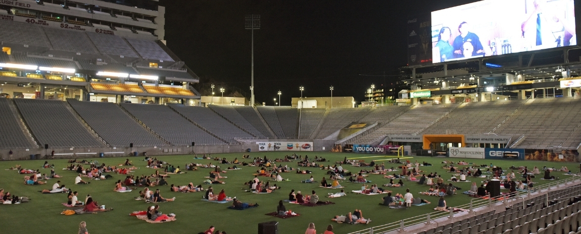 A dark stadium playing a movie on the stadium video board fills the background of a wide image