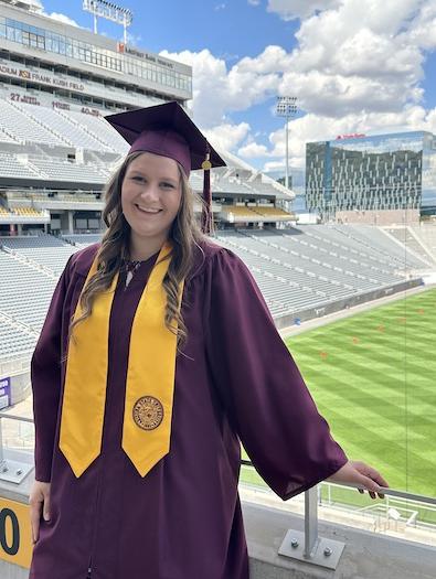 female student in cap and gown smiling at the camera with Sun Devil Stadium in the background