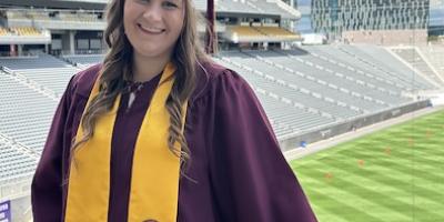 female student in cap and gown smiling at the camera with Sun Devil Stadium in the background