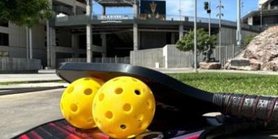 Yellow whiffle-style balls stacked between two small flat paddles balance in front of Sun Devil Stadium